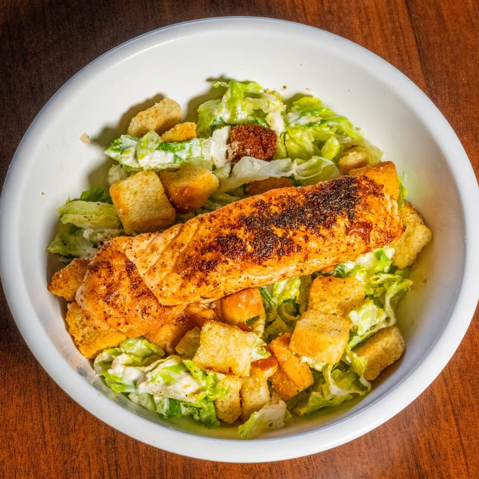 Grilled salmon fillet on a Caesar salad with croutons in a white bowl at Scores on 33rd.