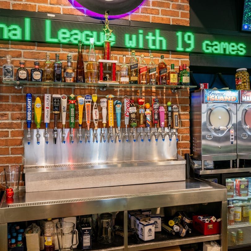 A bar at Scores on 33rd with beer taps, liquor bottles, and frozen drink machines against a brick wall.
