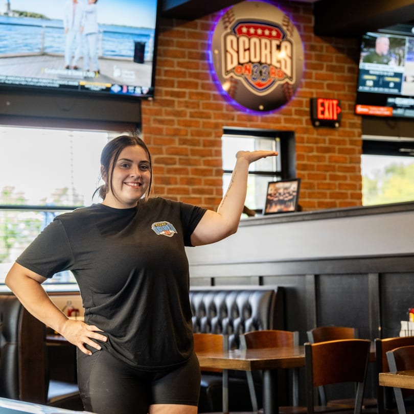 A smiling Scores on 33rd employee in a black shirt gestures towards the restaurant's interior.