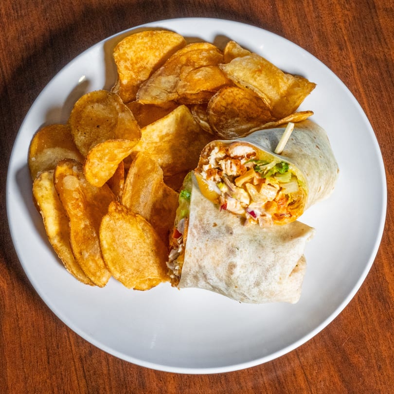 A chicken wrap with a side of potato chips on a white plate at Scores on 33rd.
